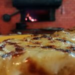 Imagen de una pizza al tacho frente al horno a leña