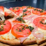 Pizza redonda con muzzarella, jamón, tomate en rodajas y albahaca